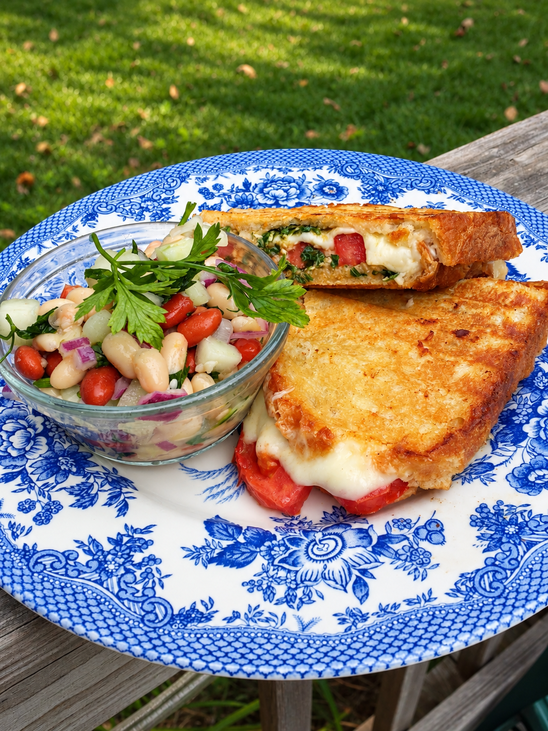 Outdoor plate with a toasted tomato and mozzarella sandwich beside white-bean salad
