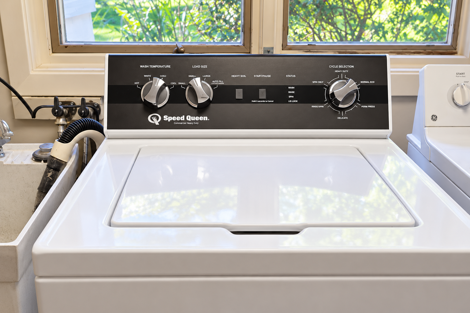 White Speed Queen top-load washer beside a utility sink