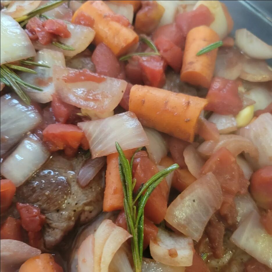 Beef shanks nestled beneath onions, carrots, tomatoes, and rosemary